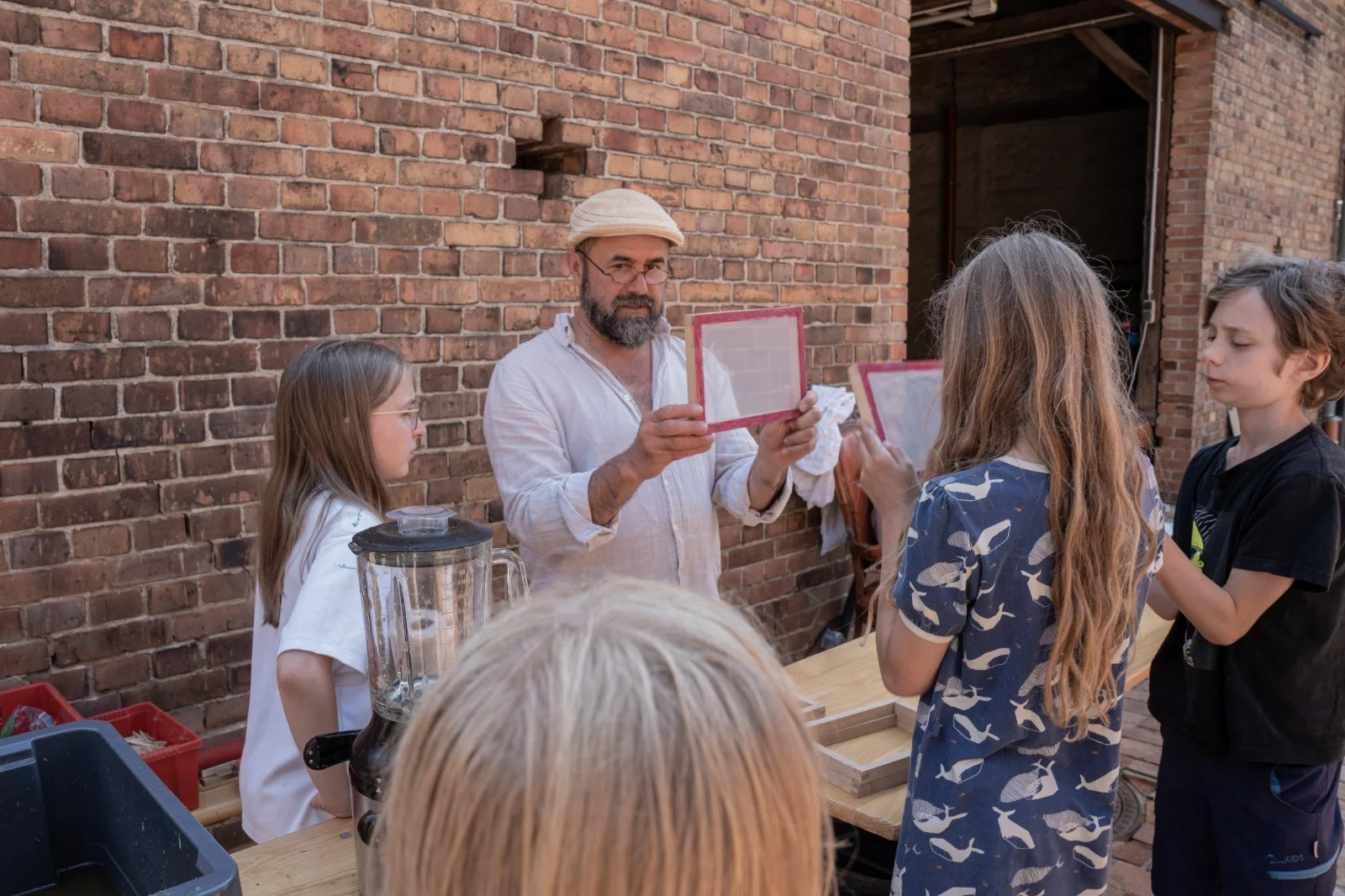 Ein Schöpfrahmen mit frisch geschöpftem Papier wird der Kindergruppe gezeigt