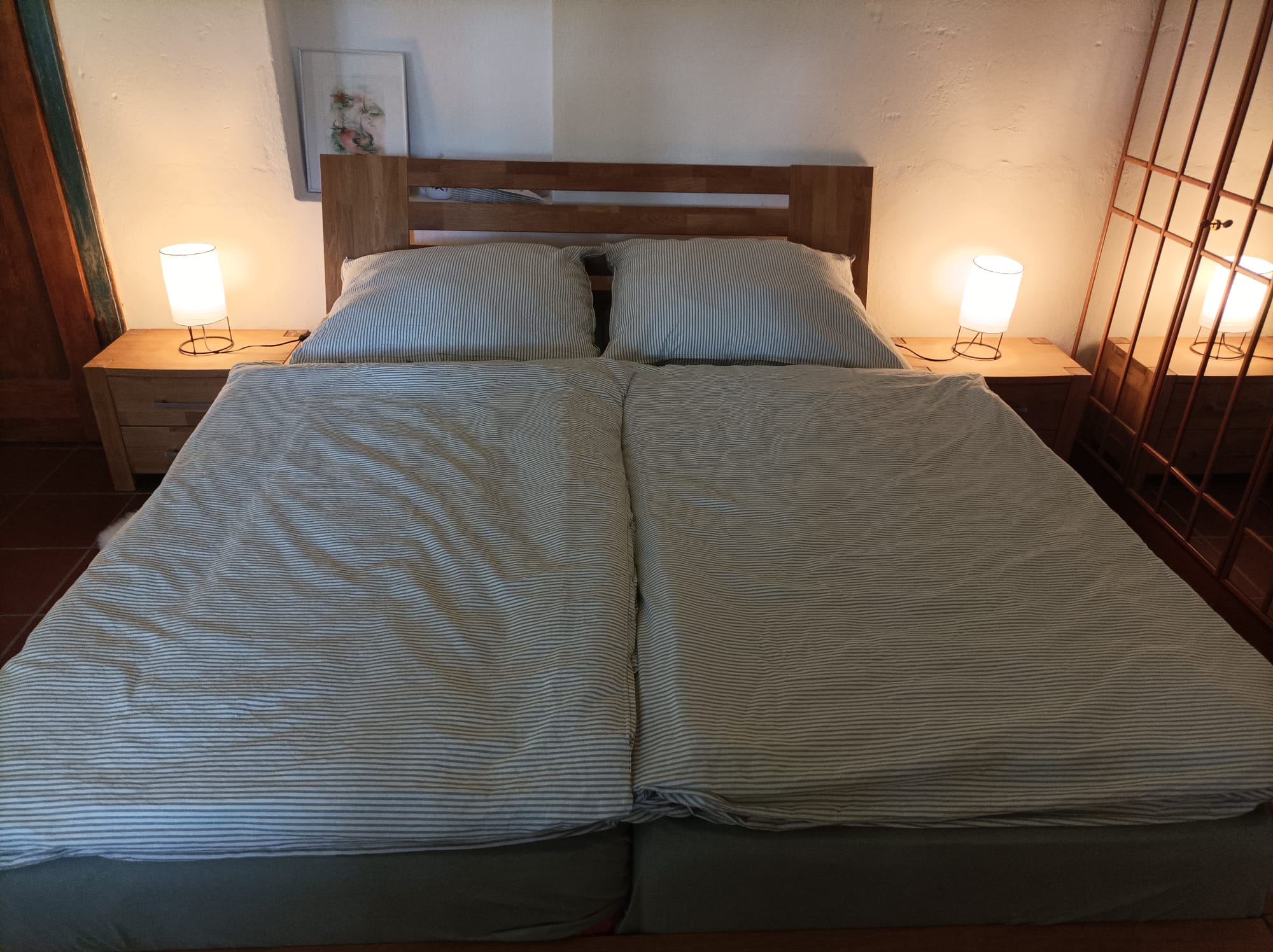 Doppelbett mit gestreifter Bettwäsche und zwei Nachttischlampen im Zimmer Kalinka