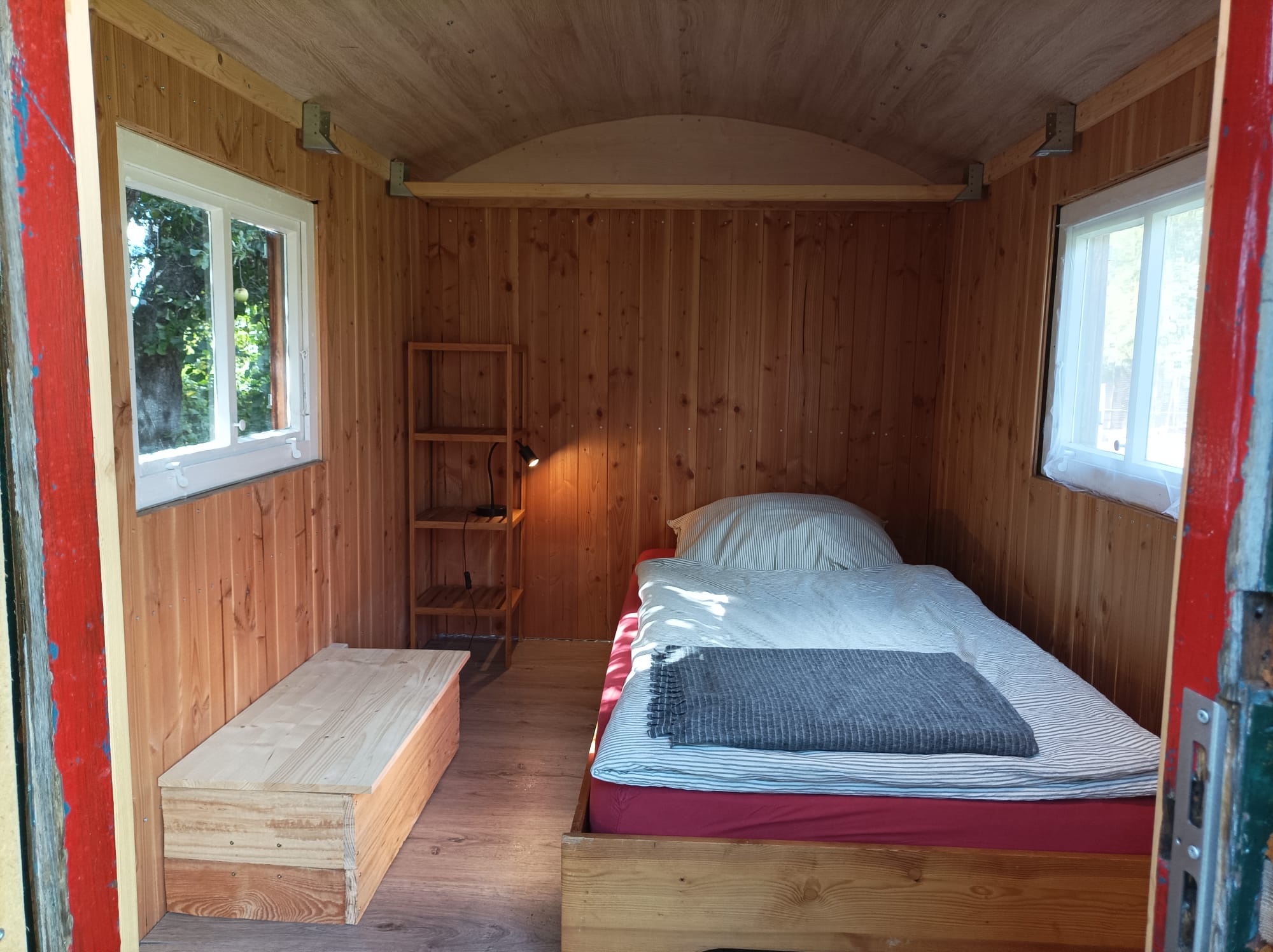 Innenansicht des Schäferwagens mit Holzverkleidung, Einzelbett und zwei Fenstern